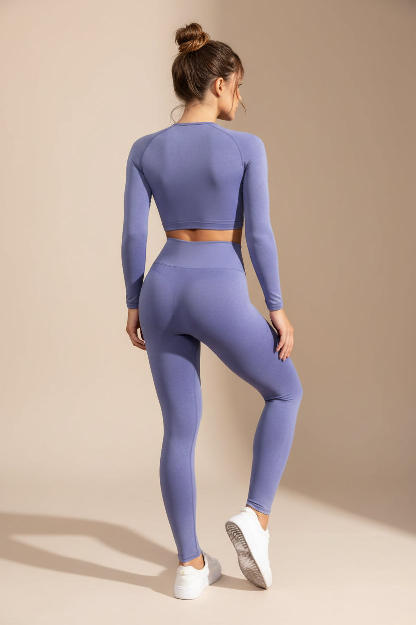 Woman wearing a purple athletic outfit standing against a gray wall.