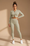 Woman wearing a light green athletic outfit standing against a gray wall.
